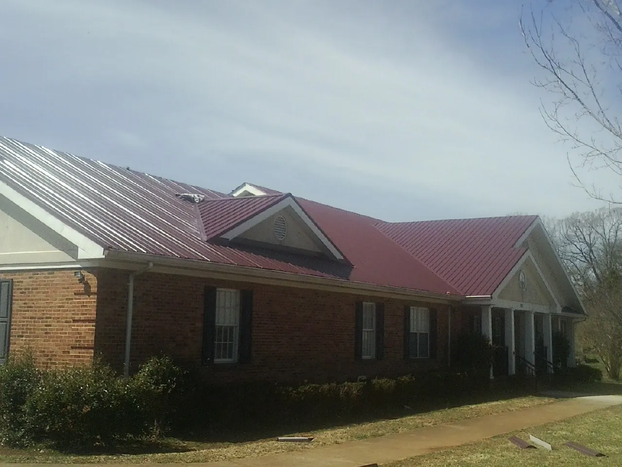 Red metal roof with gabled entries on a long brick building, from a Hail Damage Roof Repair job in Pawling