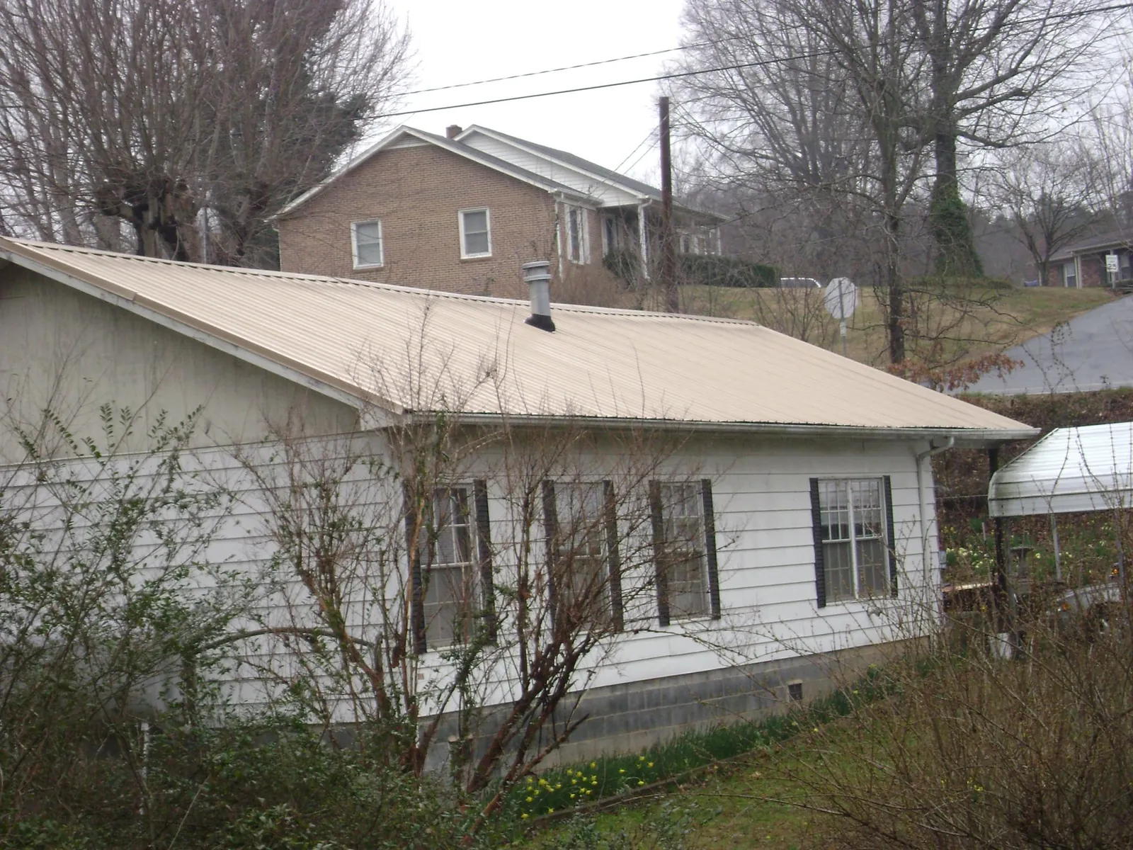 Tan metal roof on a white sided house set into a hillside — Commercial Roofing by Roofing Brothers in Pawling